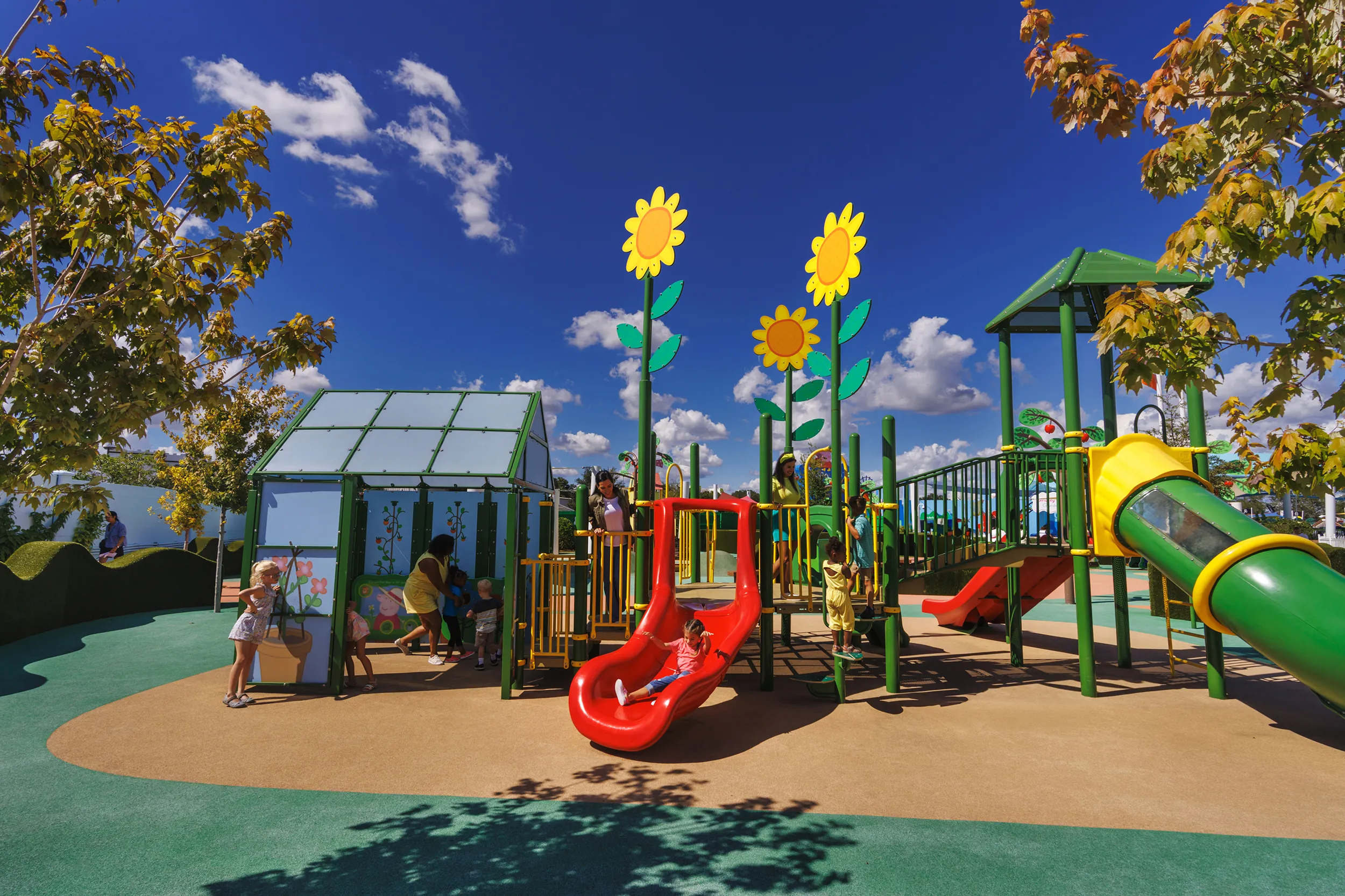 Las familias disfrutan jugando en la atracción del Invernadero de Abuelo Pig en Peppa Pig Theme Park en Dallas Fort Worth. Los niños exploran el colorido y interactivo invernadero, interactuando con las plantas y características juguetonas, mientras que los padres sonríen y disfrutan de la animada atmósfera del parque.