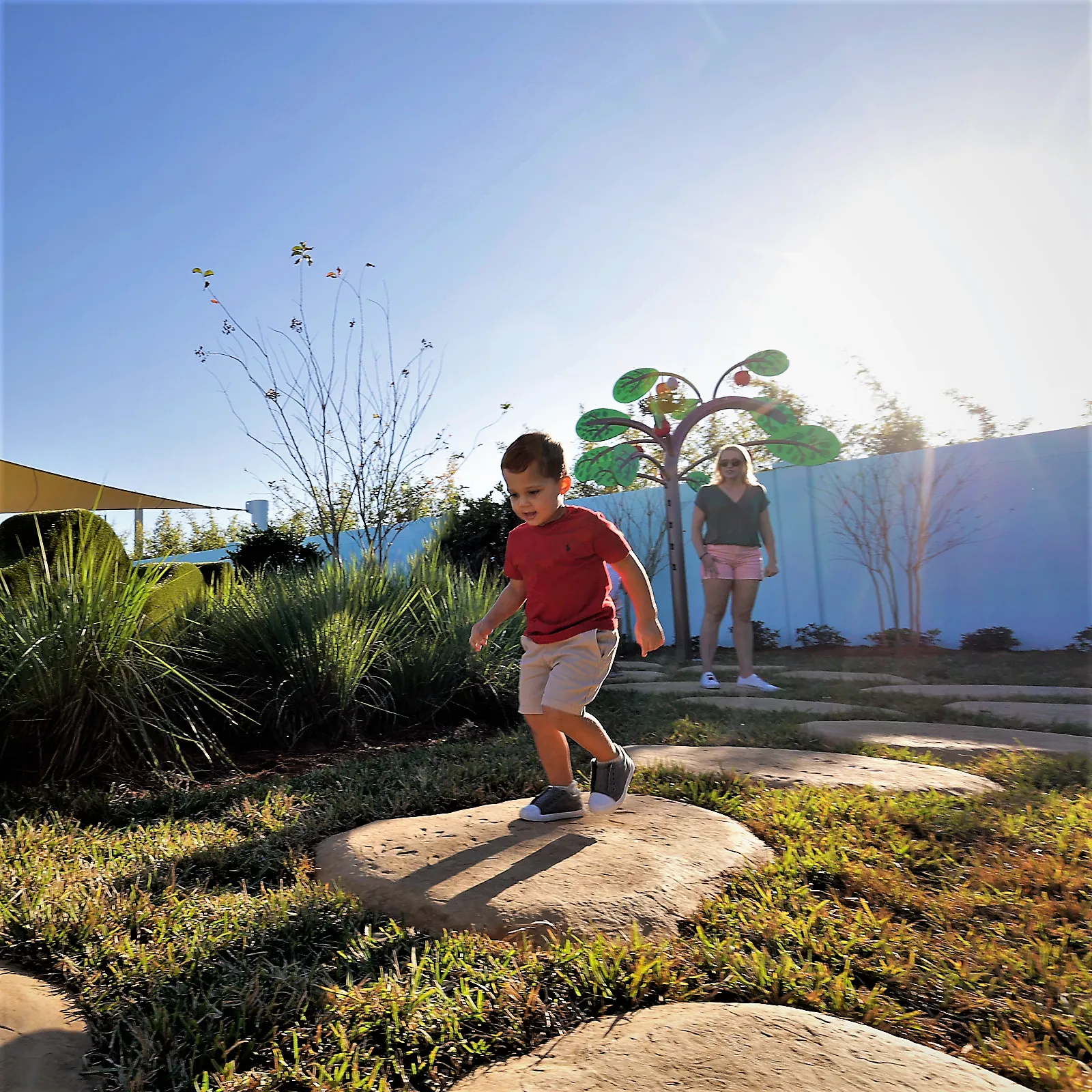 A mother and son play together at Madame Gazelle's Nature Trail attraction at Peppa Pig Theme Park in Dallas Fort Worth. They enjoy exploring the colorful and interactive nature trail, discovering fun features while surrounded by the vibrant, outdoor atmosphere of the park.