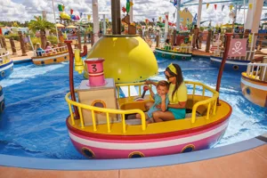 Las familias disfrutan del paseo en el Barco Pirata de Abuelo Dog en Peppa Pig Theme Park en Dallas Fort Worth. Las familias sonríen y se ríen mientras navegan en el colorido barco con tema pirata, disfrutando del ambiente divertido y aventurero del parque.