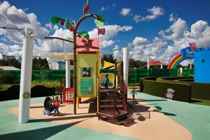 Una madre y su hijos juegan juntas en la atracción de la Casa del Árbol de Peppa Pig en Peppa Pig Theme Park en Dallas Fort Worth. Sonríen mientras exploran la colorida y interactiva casa del árbol, disfrutando del juego divertido e imaginativo en la vibrante atmósfera del parque.