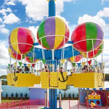 Parents and children enjoy riding Peppa Pig's Balloon ride at Peppa Pig Theme Park in Dallas Fort Worth. The family smiles and laughs as they gently soar through the air, taking in the colorful, whimsical atmosphere of the park from above.