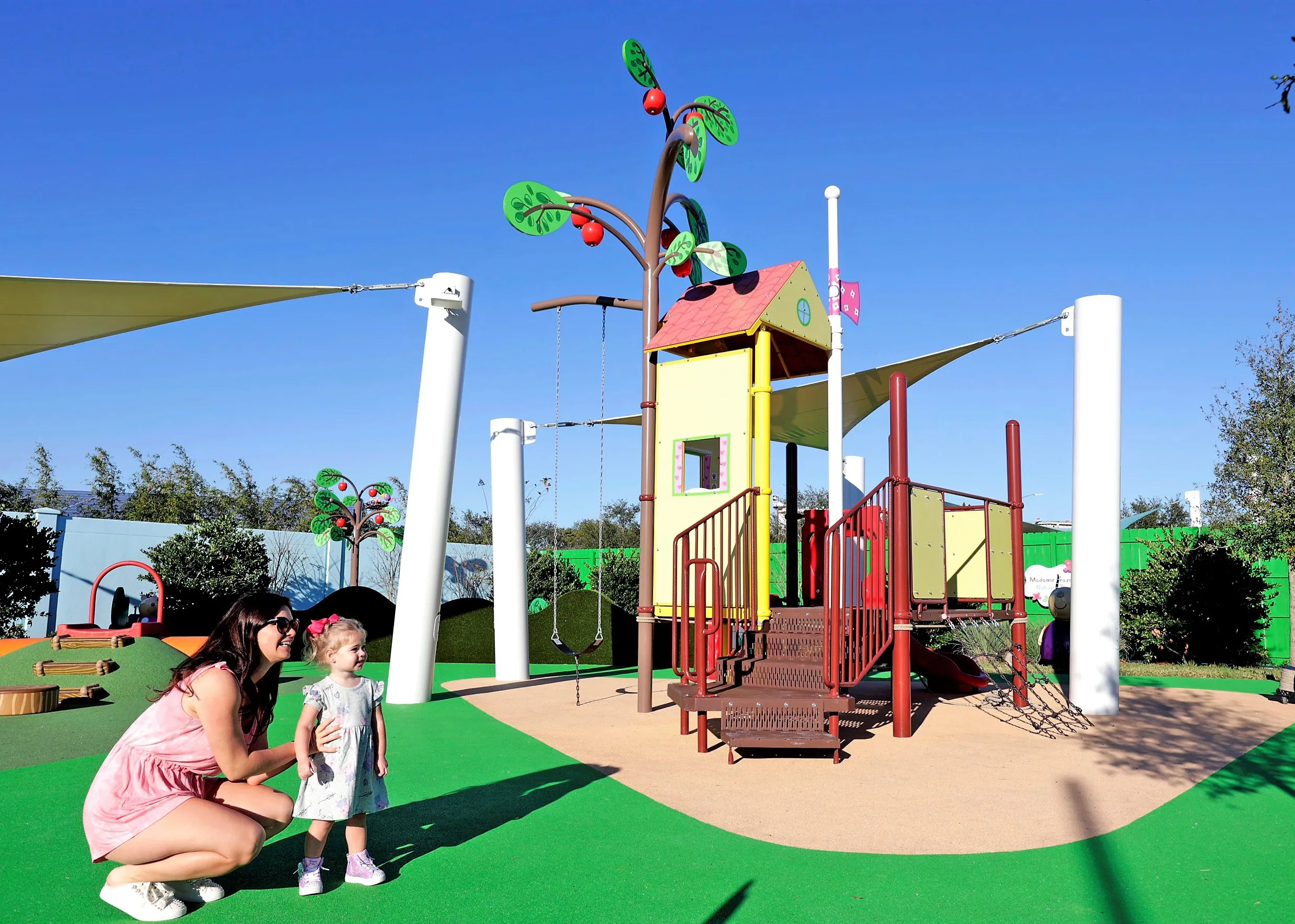 Una madre y su hija juegan juntas en la atracción de la Casa del Árbol de Peppa Pig en Peppa Pig Theme Park en Dallas Fort Worth. Sonríen mientras exploran la colorida y interactiva casa del árbol, disfrutando del juego divertido e imaginativo en la vibrante atmósfera del parque.